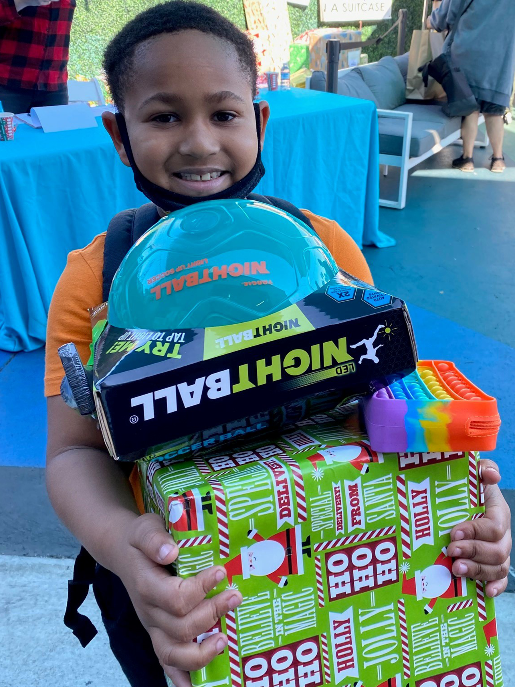 Hope in a Suitcase Child holding donated gifts including toys and wrapped boxes.